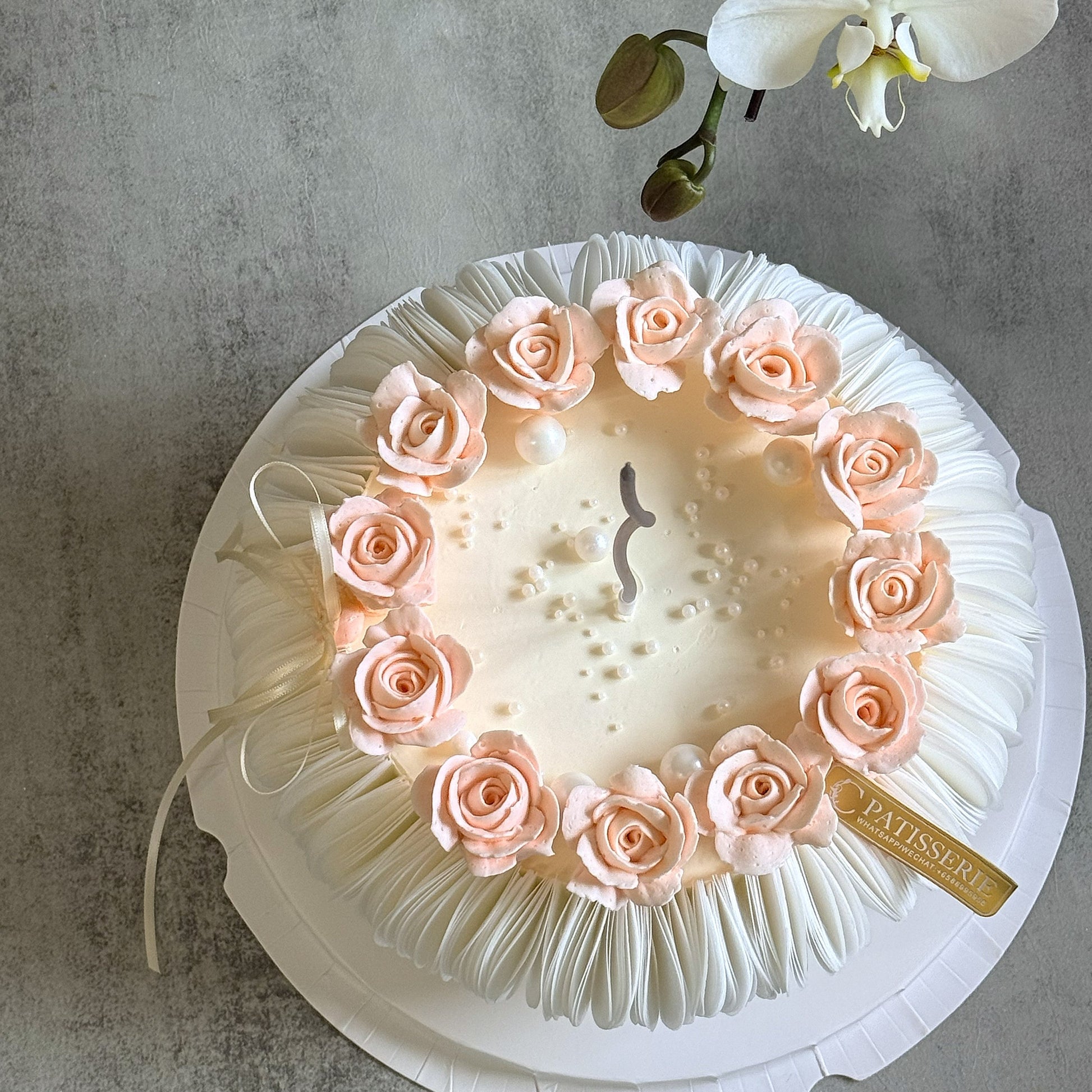 A round white cake decorated with pale pink buttercream roses and edible wafer paper around the edge. 